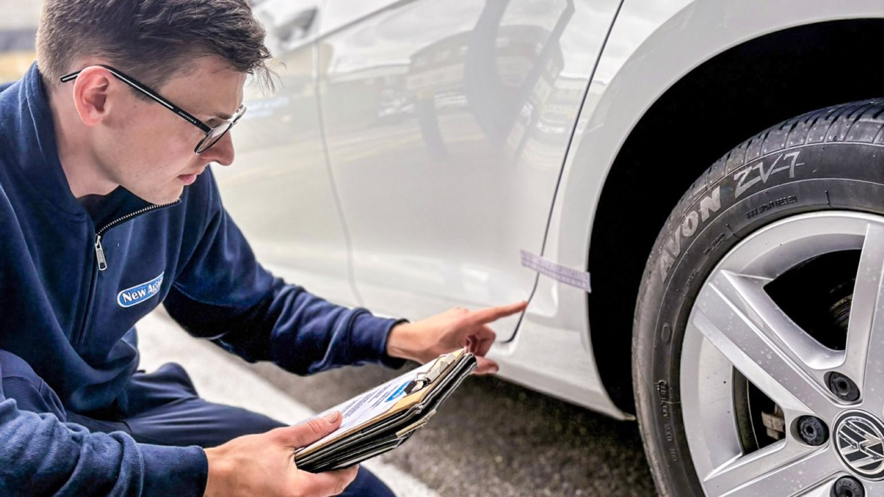 Matt from New Again inspecting a wheel arch during a lease return walkaround, ruler held against the panel