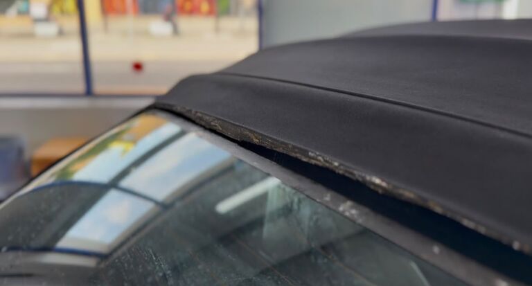 Close-up of a convertible rear window bonding seam with the old adhesive failed along the glass-to-hood join