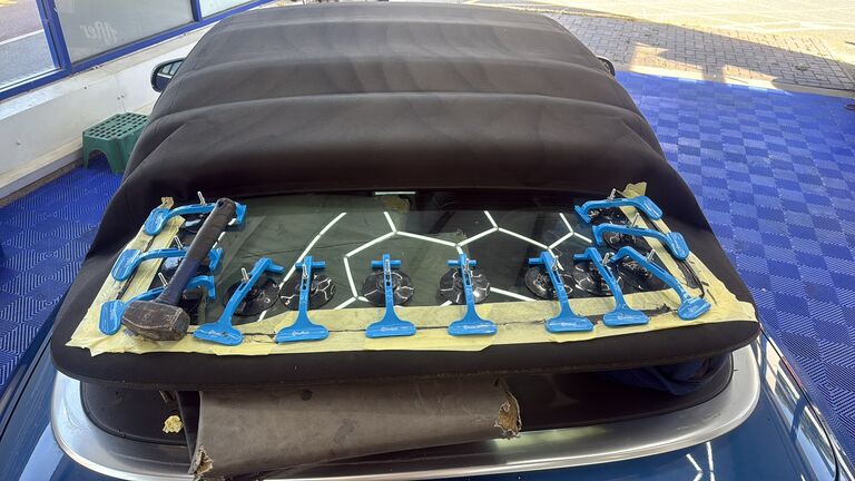 Convertible rear glass clamped with suction spreaders while heat-rated adhesive cures during a rebond in the New Again workshop