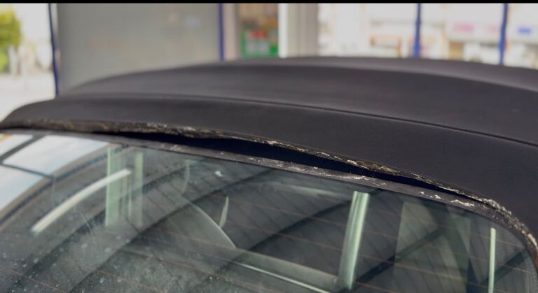 Convertible rear window debonded from the black fabric hood, the adhesive seam lifted and degraded in the heat